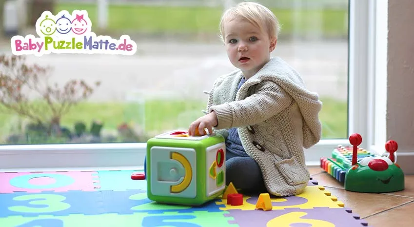 Kleinkind oder Baby Puzzleatte mit Spielzeug vor Fenster