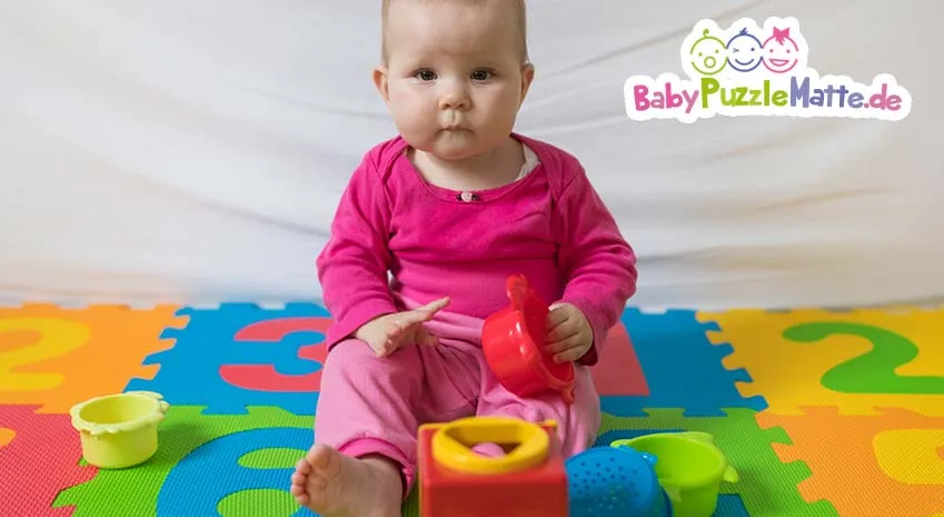 Baby in rosa Strampler spielt auf eine Puzzlematte wie von Prinzbert 