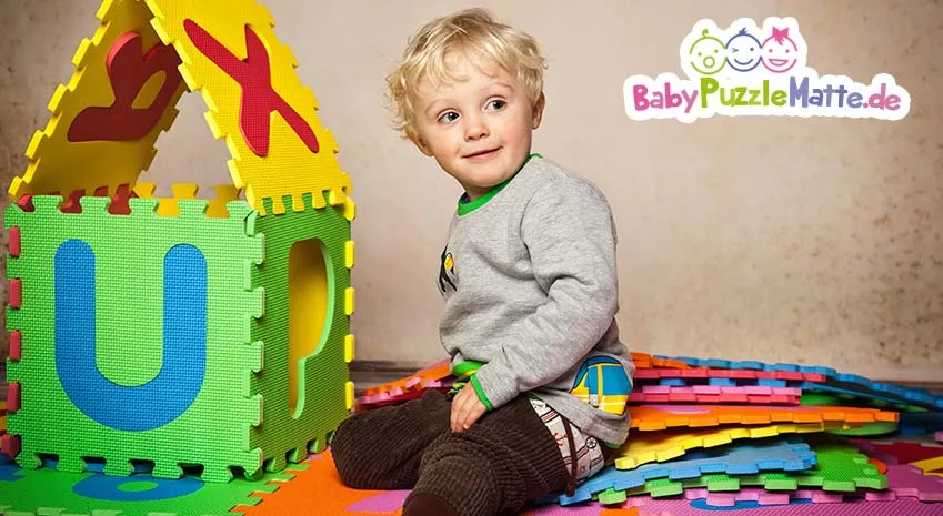kleiner Junge baut aus Puzzlematte ein Häußchen